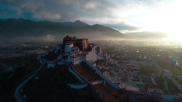 Aerial view of the Potala Palace at sunrise in Lhasa, Tibet, China, with the historic palace on the hill overlooking the city, surrounded by mountains and morning mist under golden light.