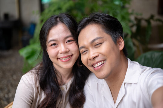 Close up shot of smiling asian man and woman couple enjoying time together in green garden at cafe.