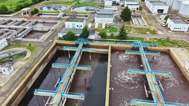 Aerial sewage treatment plant with aerators showing clarifier basins and bubbling effluent drone view captures piping network, industrial buildings, green