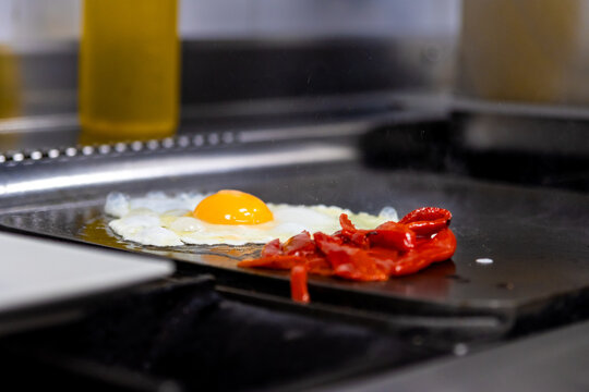 Preparing fried egg and roasted red peppers on a hot griddle in a commercial kitchen