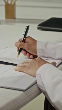 Vertical video of male engineer opening folder and signing document with pen. Footage represents corporate legal agreements or energy sector compliance