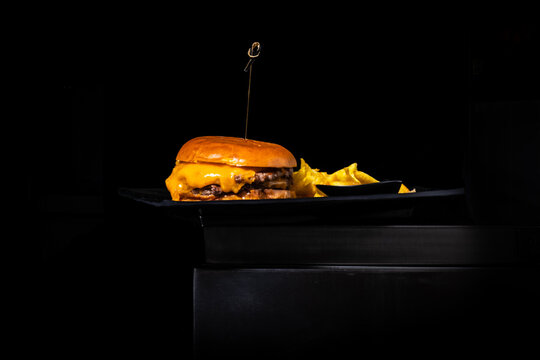 Double cheeseburger with crispy chips served on a restaurant plate against a dark background