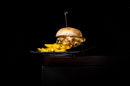 Gourmet cheeseburger with caramelized onions and fries served on dark background