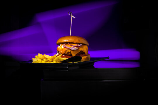 Gourmet cheeseburger and fries plate against neon purple light in a restaurant