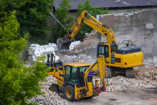 View of two yellow excavators demolishing an old building with dust and rubble on a construction site in Vilnius, Vilnius County, Lithuania.