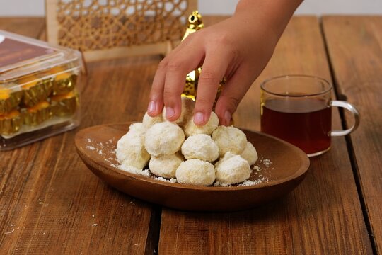 Hand taking Kue Putri Salju or powdered sugar cookies from plate showing interaction.