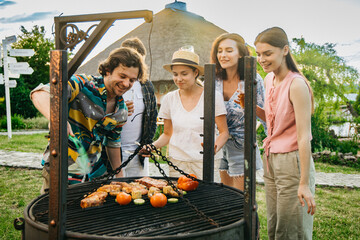 Obraz premium Group of friends grilling barbecue outdoors during a summer picnic. Concept friendship, outdoor cooking and leisure. 