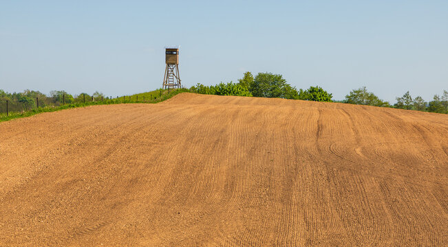 View of a wooden hunting tower standing on a grassy hill overlooking a freshly plowed brown field under a clear blue sky Stanczyki, Warmian-Masurian Voiv, Poland.