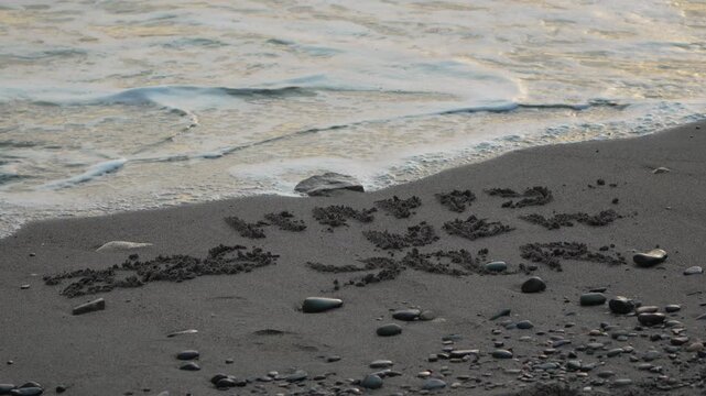 Sand wave erasing message written in dark beach sand. Happy new year holiday greeting concept.