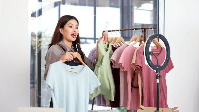 Young asian entrepreneur  live online clothing store while showing clothing with tablet on social at home, entrepreneur streaming for selling online clothing and presenting, online seller.