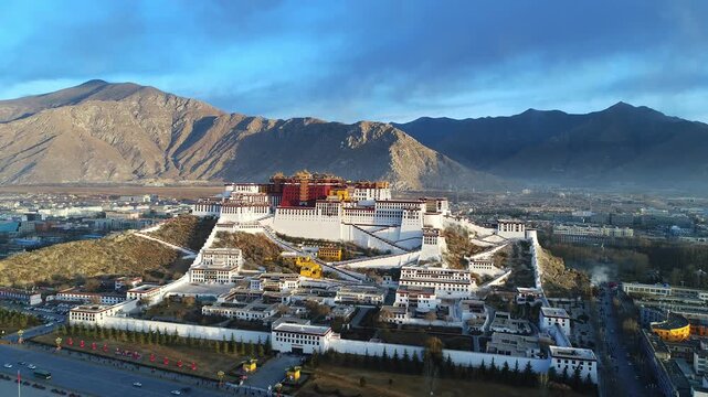 Aerial view of the Potala Palace at sunrise in Lhasa, Tibet, China, with the historic palace on the hill overlooking the city, surrounded by mountains and morning mist under golden light.