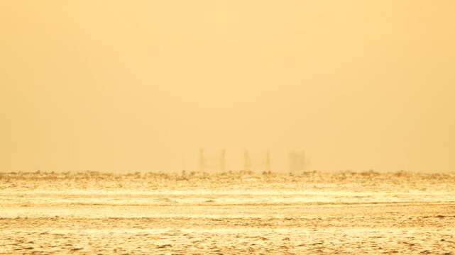 Ocean mirage horizon shimmering heat haze over the sea at sunset with distant industrial structures and a flying bird