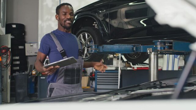 Experienced auto mechanic, illuminating the engine with a flashlight, and explaining to the client the defect in her vehicle.