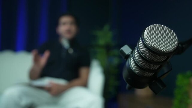 Extreme close up of a dynamic studio microphone with a blurry male speaker talking in the background. Perfect for podcasting, broadcasting, and audio production concepts