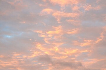 Fototapeta premium Soft pastel clouds illuminated by sunset light in a colorful evening sky. Atmospheric cloudscape background with warm tones, natural beauty and ample copy space.