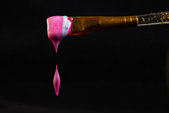 Pink paint drop falling from paint brush