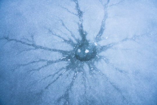 View of intricate ice cracks radiating from a central point on a frozen lake surface along the Icefields Parkway Jasper, Alberta, Canada.