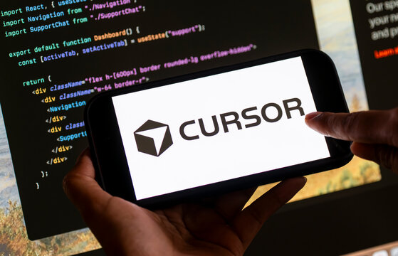 In this photo illustration, The Cursor AI logo is displayed on a smartphone screen in front of computer code and a software development interface
