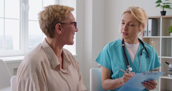 Doctor and senior patient in consultation at medical clinic. A nurse with stethoscope writes on a clipboard, discussing symptoms, diagnosis, and treatment. Medicine, compassionate healthcare service.