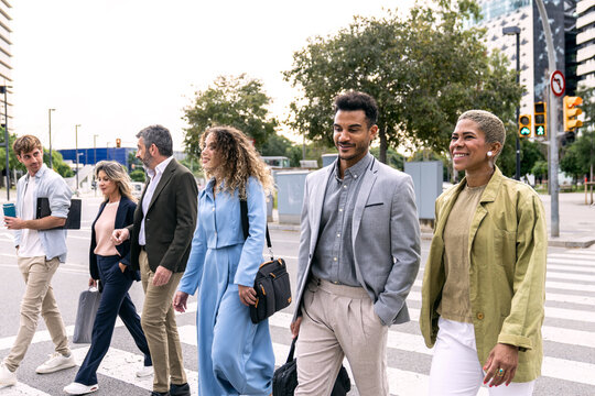 Group of business people, males and females, walking together on a pedestrian crossing in an urban setting