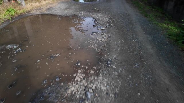 A cinematic 4K 24fps handheld shot of a muddy water puddle on a rough dirt road. Dynamic camera movement creates a realistic motion blur effect, capturing a gritty, realistic rural atmosphere.