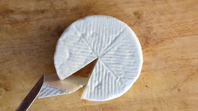Top view of a person cutting a wheel of traditional white goat cheese on a rustic wooden board, gourmet food preparation and artisan cheese making concept in a Mediterranean kitchen