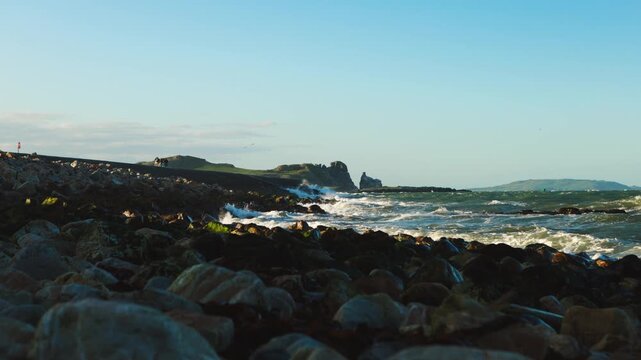 People Walking Along Howth Pier as Waves Crash Against the Rocky Shore