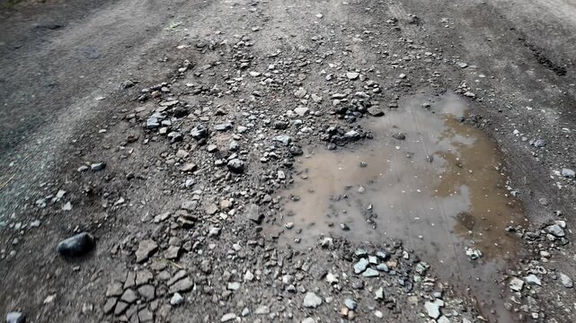 A cinematic 4K 24fps handheld shot of a muddy water puddle on a rough dirt road. Dynamic camera movement creates a realistic motion blur effect, capturing a gritty, realistic rural atmosphere.