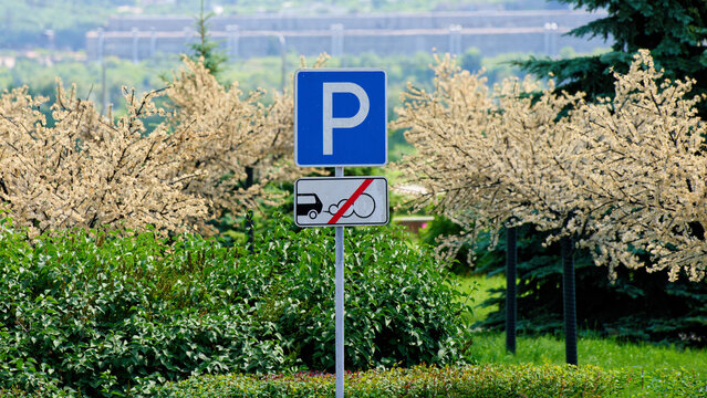 Traffic signage marking car parking where engines must be off, set amid decorative trees and hedges. Urban air pollution control and eco policy message. Photo
