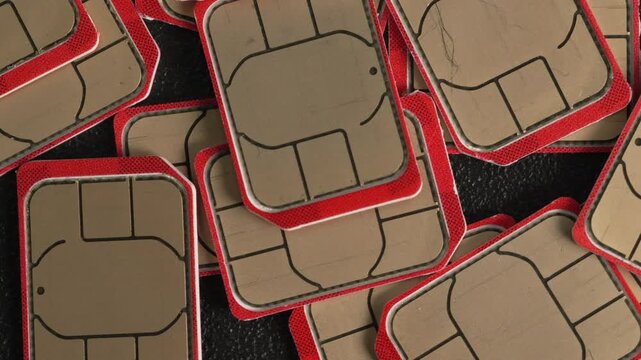 A scattered collection of SIM cards with red edges displayed on a textured black surface. Useful for technology-themed presentations or telecommunications content.