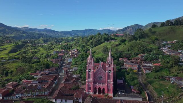 Aerial view pulls back from pink Gothic church to reveal lush hills and townscape