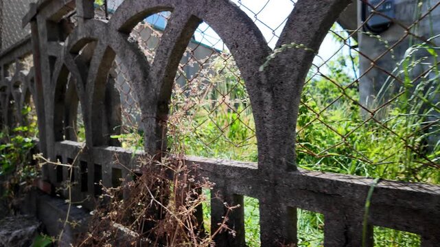 A cinematic 4K 24fps panning shot of an old textured concrete fence overgrown with wild grass. Fast camera movement creates realistic motion blur, capturing a gritty, rural summer atmosphere.