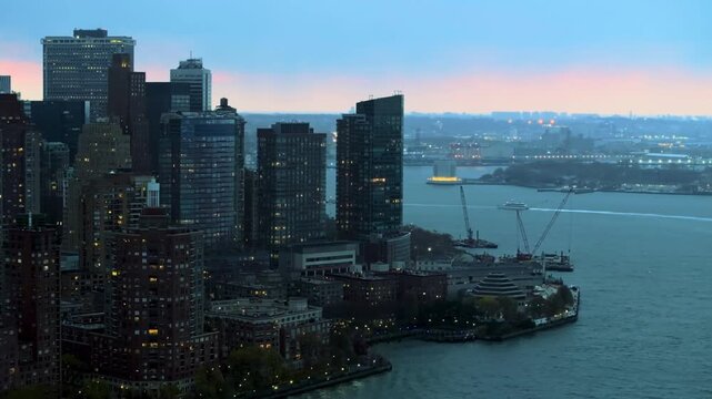 A breathtaking wide aerial shot of Manhattan, showcasing the iconic New York City skyline alongside the surrounding river. Towering skyscrapers rise above the waterfront as the expansive cityscape str