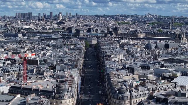 Soaring above Paris as the drone climbs and pushes forward, tilting down to capture a spectacular view of an iconic roof statue and the bustling avenue below.