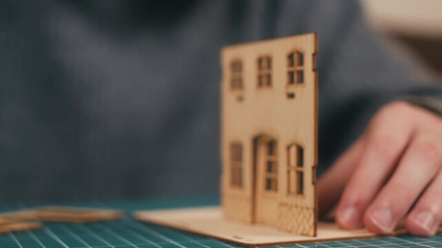 Positioning wooden wall panel in miniature house model assembly. DIY architecture crafting featuring plywood construction and precise handcrafted building process. Fresh homeownership concept
