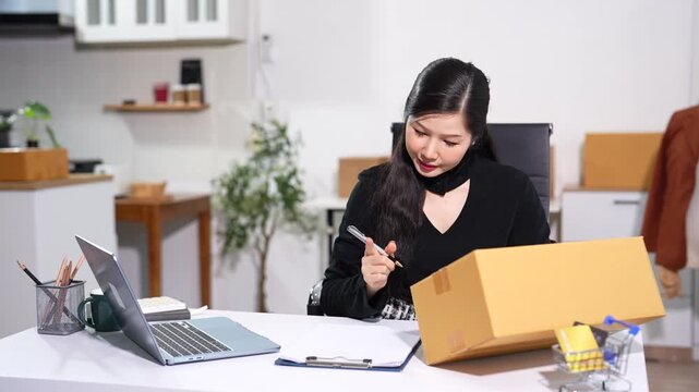 Asian woman small business owner packing shipping boxes for online store startup.