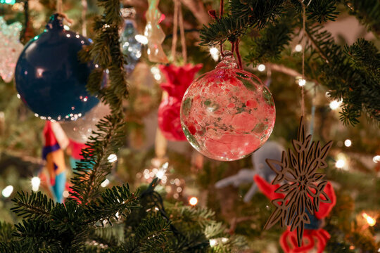 Colorful Christmas tree ornaments hanging on a green pine with twinkling lights.