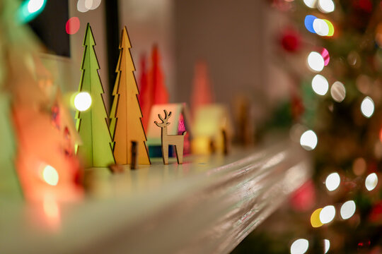 Colorful paper trees and a reindeer adorn a festive mantel with blurred holiday lights.