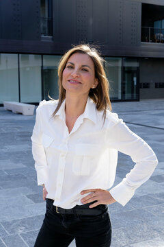 Woman in white shirt and black pants smiles confidently outdoors in urban setting. Milan, Italy