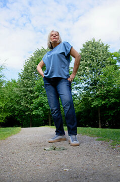 Woman posing confidently on a forest path with trees and blue skies in the background.
