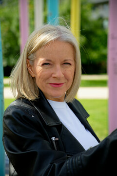 Mature woman in black jacket smiling outdoors with colorful background elements.