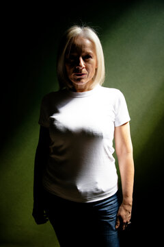Woman in a white shirt stands against dark, green background with dramatic lighting.