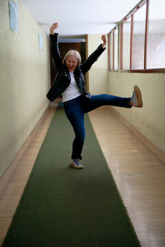Energetic woman joyfully dancing in a corridor with green carpet and beige walls.