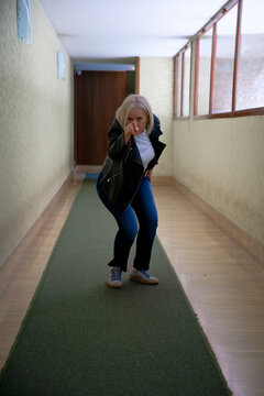 Person wearing a black jacket crouching and pointing in a narrow hallway.