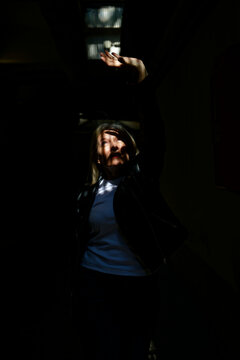 Woman in dim light shields eyes, creating intriguing shadows on her face and body.
