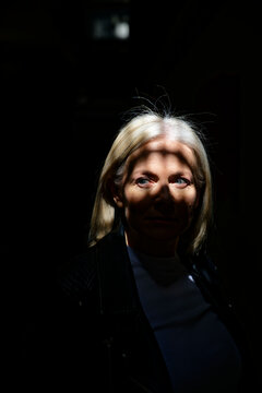Woman with blonde hair stands in dramatic lighting, casting shadows on her face.