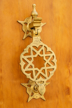 Intricate brass door knocker with geometric patterns on a wooden door.