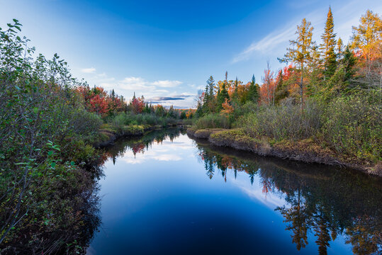 Tranquil river reflecting autumn trees and clear blue sky in a serene natural landscape.