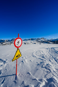 Snowy landscape with warning signs against a bright blue sky and distant mountains.