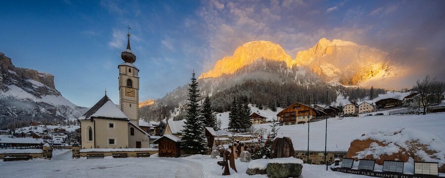 Scenic winter village with church and snowy mountains bathed in golden sunset light.